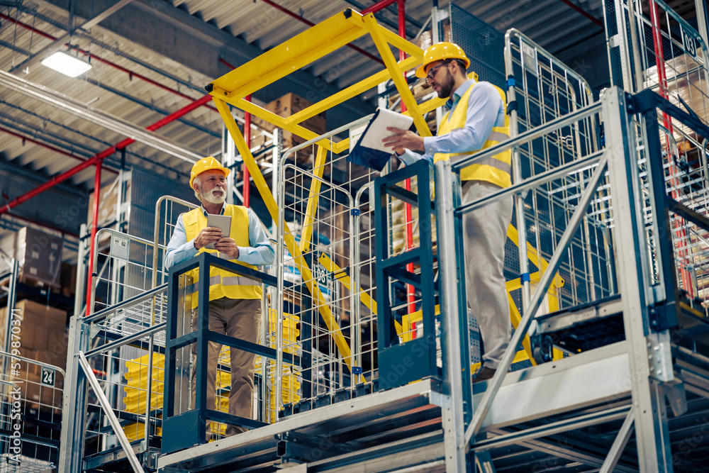 Two successful smiling business man walking through big warehouse and checking documents