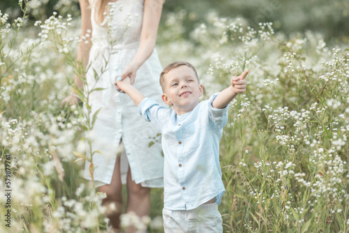 Beautiful young mother walking with her young son on the daisies field. mom holds him gently by the hand, hugs and throws up in the sky. Portrait of young man