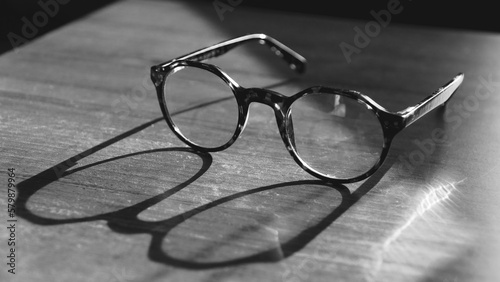 Glasses on wooden table. Sunshine reflecting on vintage glasses on the table. Wisdom concept. Copy space for text. Black and white background