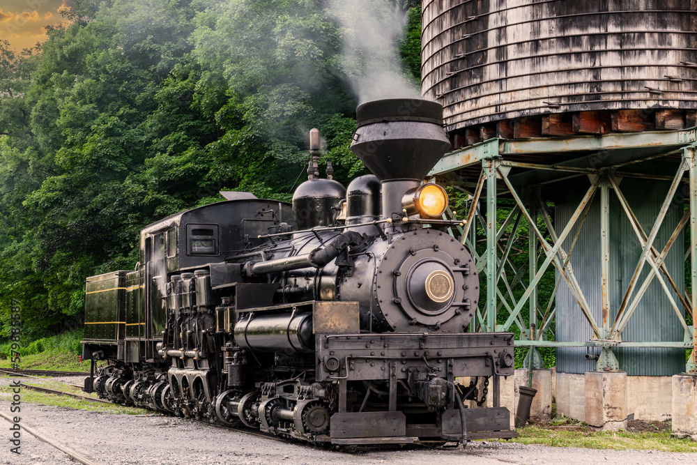 Naklejka premium An Antique Shay Steam Locomotive, Steamed up, Blowing Smoke, Sitting by a Water Tower, Getting Ready for Work