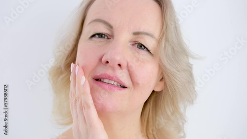 Extreme closeup feminine lips and chin applying anti aging cream on face skin. Women demonstrate moisturizing facial care touching cheek isolated on gray studio background photo