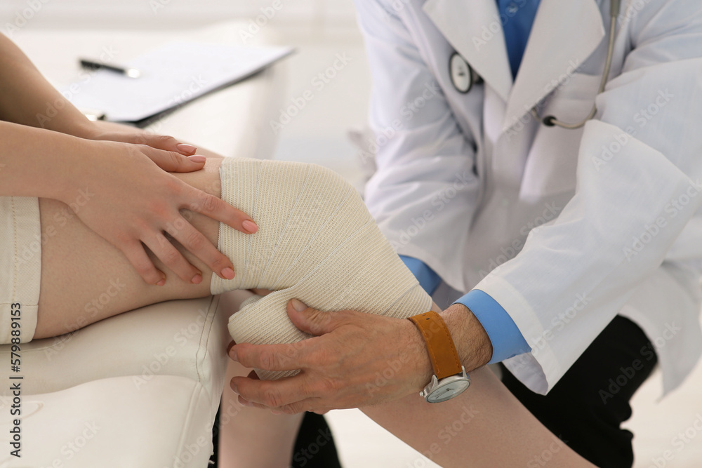 Orthopedist applying bandage onto patient's knee in clinic, closeup Orthopedist applying bandage onto patient's knee in clinic, closeup