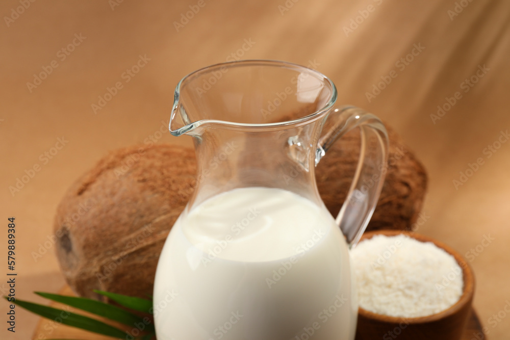 Glass jug of delicious vegan milk near coconuts on brown background, closeup Glass jug of delicious vegan milk near coconuts on brown background, closeup