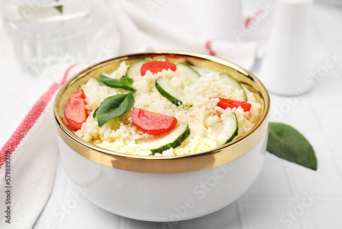 Tasty couscous with tomatoes, cucumber and basil on white tiled table, closeup