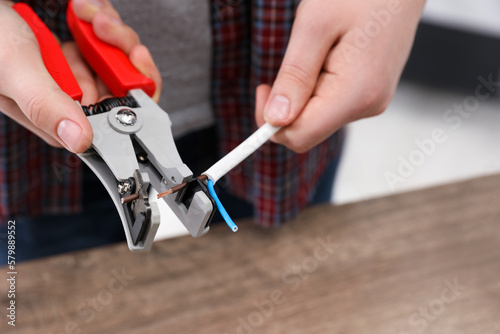 Professional electrician stripping wiring at wooden table, closeup