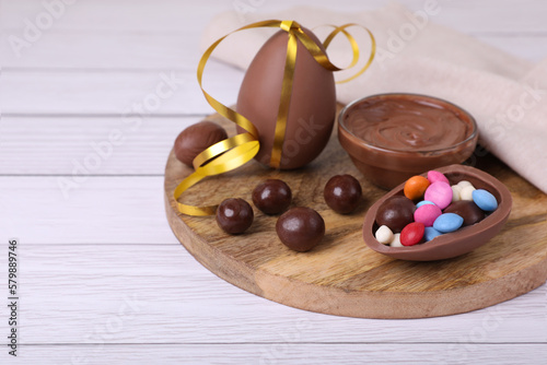 Composition with delicious chocolate eggs and candies on white wooden table. Space for text