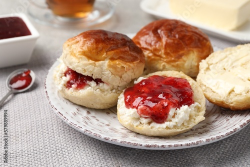 Freshly baked soda water scones with cranberry jam and butter on light grey mat, closeup