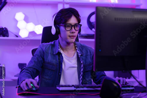 Asian gamer with a happy expression in front of a computer screen, lokking in computer screen and concentrate with online video game. Professional gamer concept