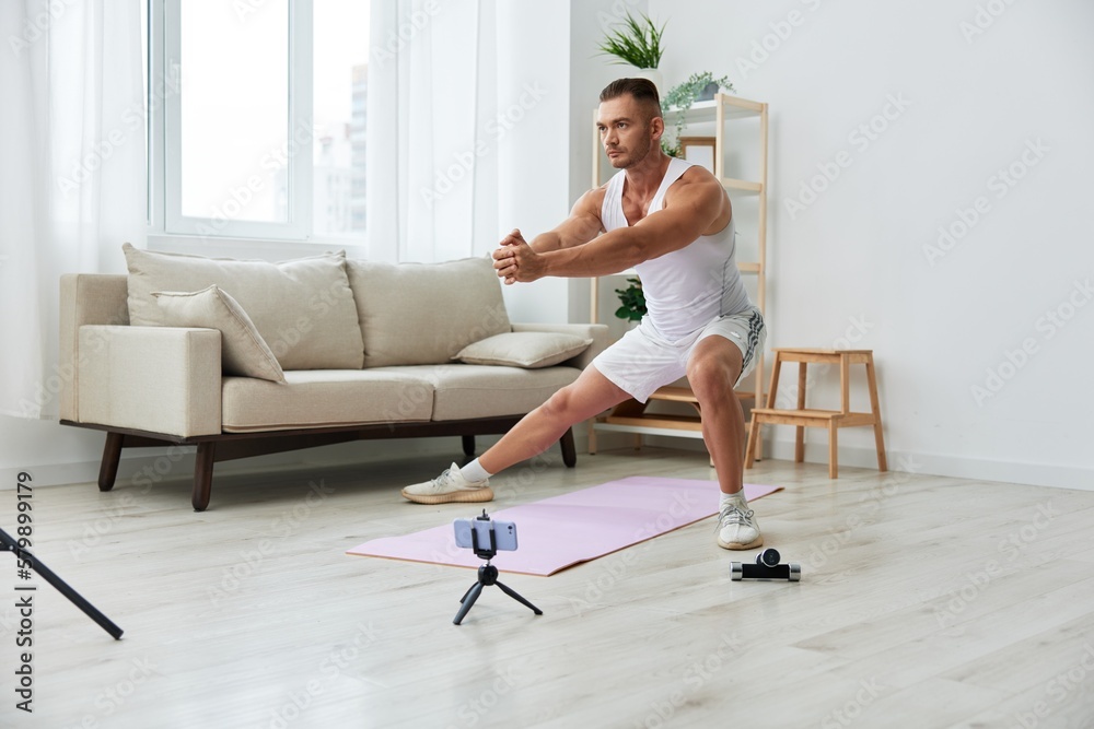 Man sports, watching a workout tape on his phone and repeating exercises blogger, pumped up man fitness trainer works out at home, the concept of health and body beauty Man sports, watching a workout tape on his phone and repeating exercises blogger, pumped up man fitness trainer works out at home, the concept of health and body beauty