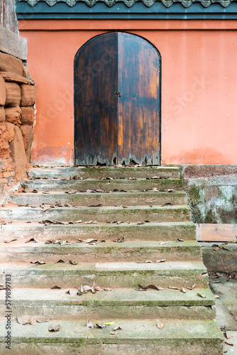 Ancient closed wooden door on a red wall with stairs in the foreground in a taoist temple, Luodai, Sichuan province, China photo