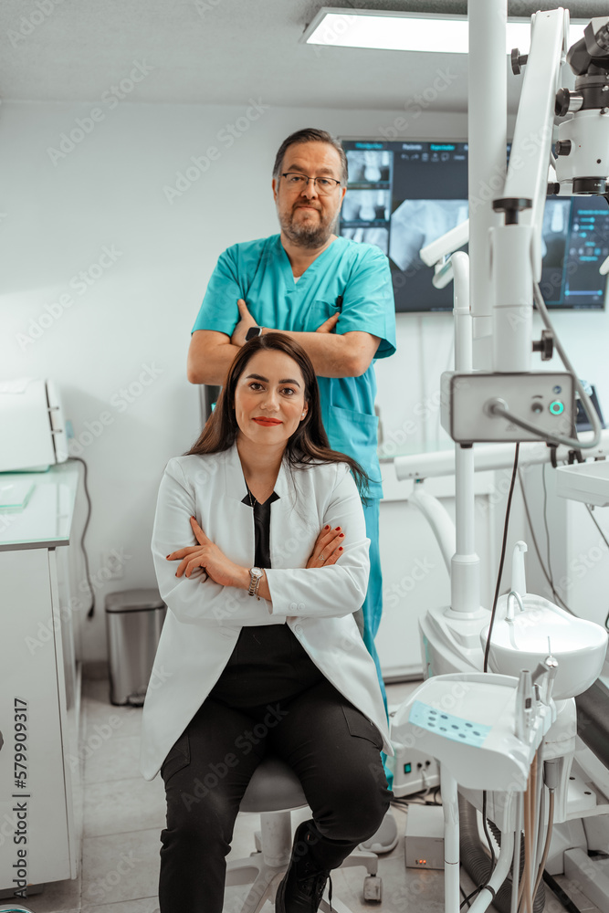 Smiling doctor and assistant with crossed hands looking at camera in dental clinic Smiling doctor and assistant with crossed hands looking at camera in dental clinic