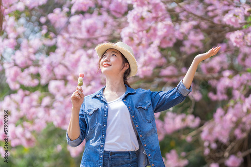 Asian woman holding the sweet hanami dango dessert while walking in the park at cherry blossom tree during spring sakura festival with copy space