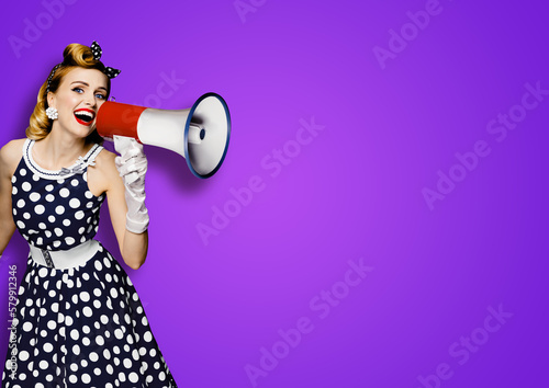 Portrait image of beautiful woman holding mega phone, shout, saying, advertising. Pretty girl in black pin up style dress with mega phone loudspeaker. Isolated violet purple background. Big sales ad.