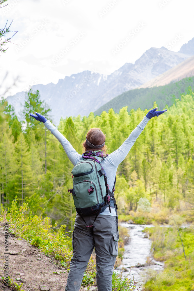 Young woman with backpack enjoys the view of nature at hike with hands up
