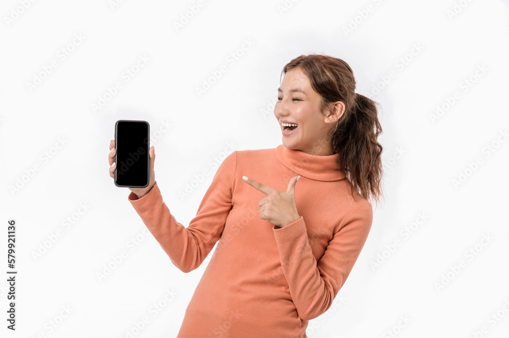 Portrait photo of young beautiful Asian woman feeling happy or surprise shock pointing at smart phone with black empty screen on white background can use for advertising or product presenting concept. Portrait photo of young beautiful Asian woman feeling happy or surprise shock pointing at smart phone with black empty screen on white background can use for advertising or product presenting concept.