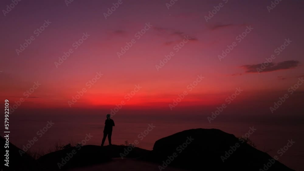 A man stands and takes a selfie against a scene with a red sky..The male silhouette in the sky and sea scene was red on the steep cliff..red sea red sky of twilight background.atmosphere pleasant. A man stands and takes a selfie against a scene with a red sky..The male silhouette in the sky and sea scene was red on the steep cliff..red sea red sky of twilight background.atmosphere pleasant.