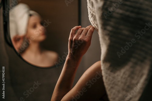 Rear view of a gorgeous woman cleaning her ear with an earbud at home. Focus on hand with a cotton swab