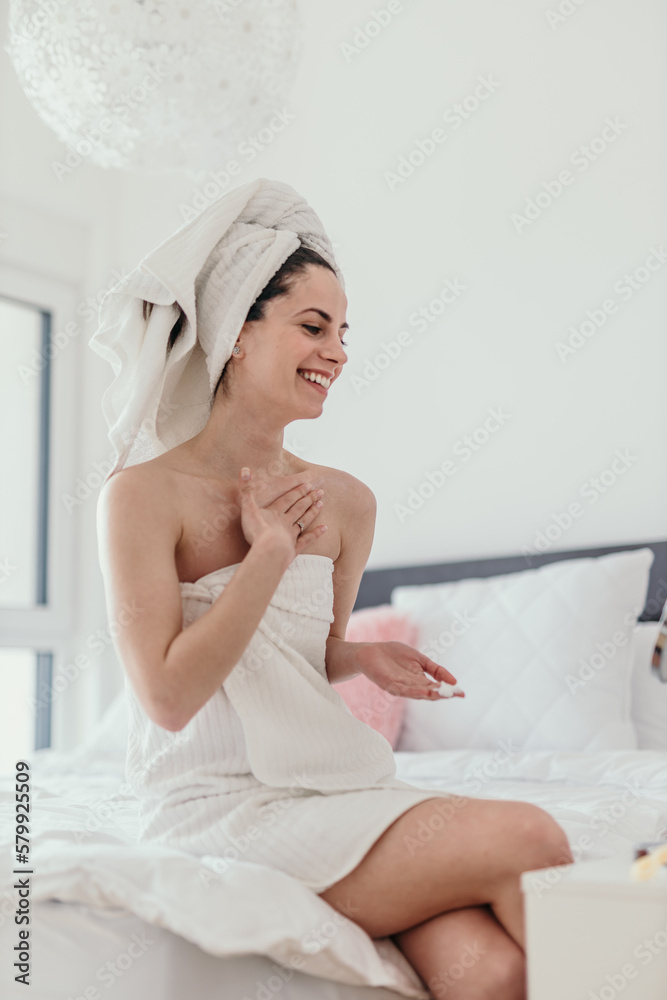 Happy woman doing routine skin care at home with beauty products. A Woman sitting on the bed at home and applying body cream. Copy space Happy woman doing routine skin care at home with beauty products. A Woman sitting on the bed at home and applying body cream. Copy space
