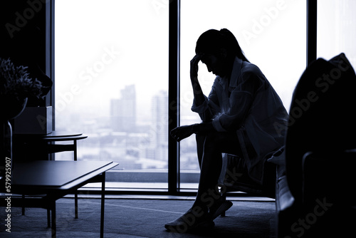 silhouette of stressed woman sitting on sofa beside the windows, The concept of depression.