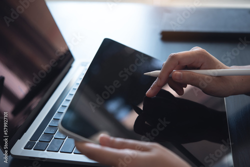 Close up, woman hand with stylus pen using digital tablet, finger touching on screen and working on laptop computer on office table, online working, business and technology, internet networking