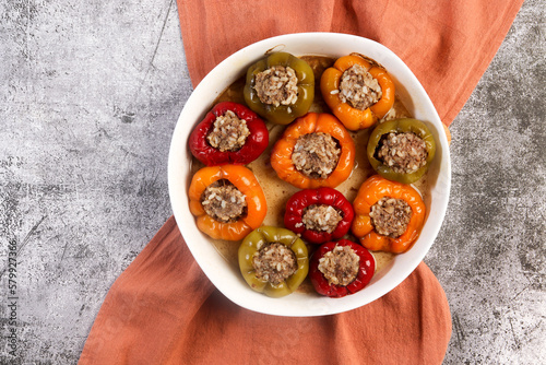 Oven baked stuffed bell peppers with ground beef and rice in a white baking dish on a dark grey background. Top view, flat lay