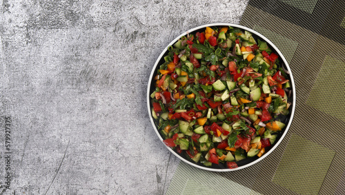 Summer homemade tomato and cucumbers salad on a round plate on a dark gray background. Top view, flat lay
