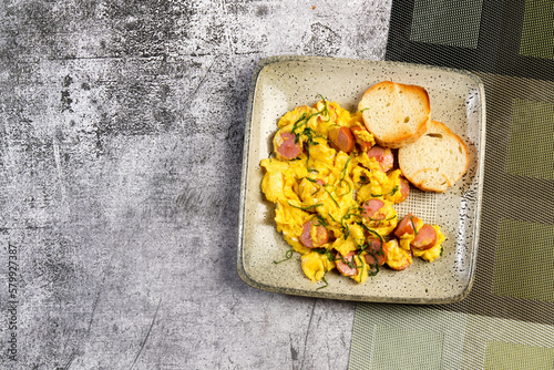 Scrambled eggs with sausages and bread toasts on a square  plate on a dark background. Top view, flat lay