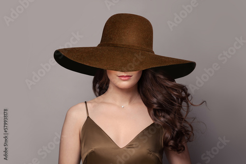 Brunette woman with wavy hair in wide brown broad brim hat. © millaf