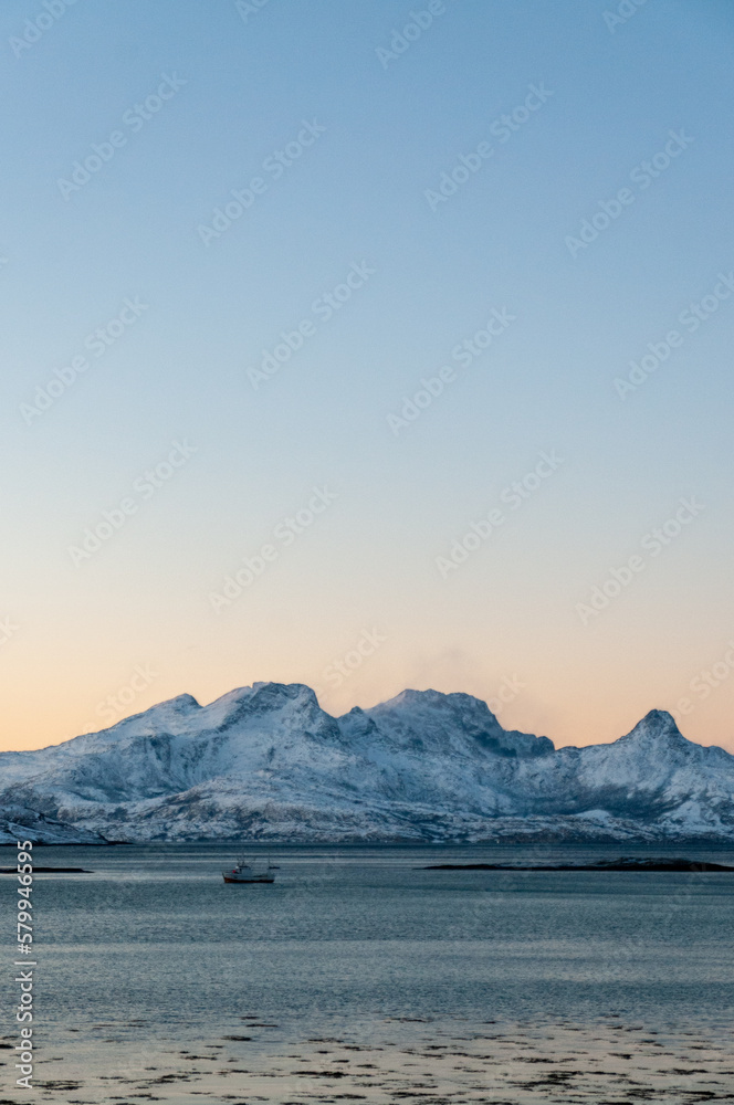Landscape shot highlighting the rugged mountains and snow-covered beaches of arctic norway during a brief golden hour during the long winters. Landscape shot highlighting the rugged mountains and snow-covered beaches of arctic norway during a brief golden hour during the long winters.