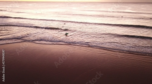 Majestic ocean sunrise with solo surfer walking in to water