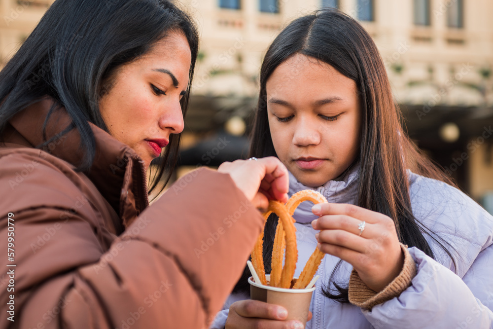 Mother and daughter eating churros with chocolate in the street, Mother and daughter eating churros with chocolate in the street,