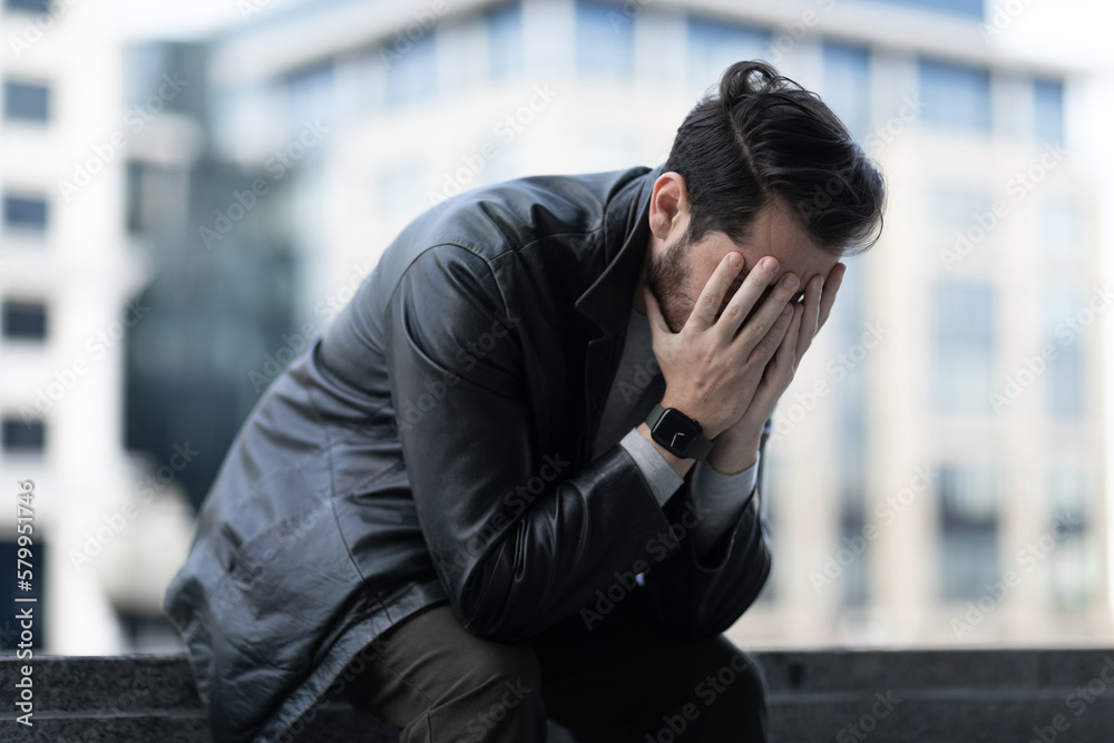 distressed middle-aged man crying with his eyes closed while sitting on the street