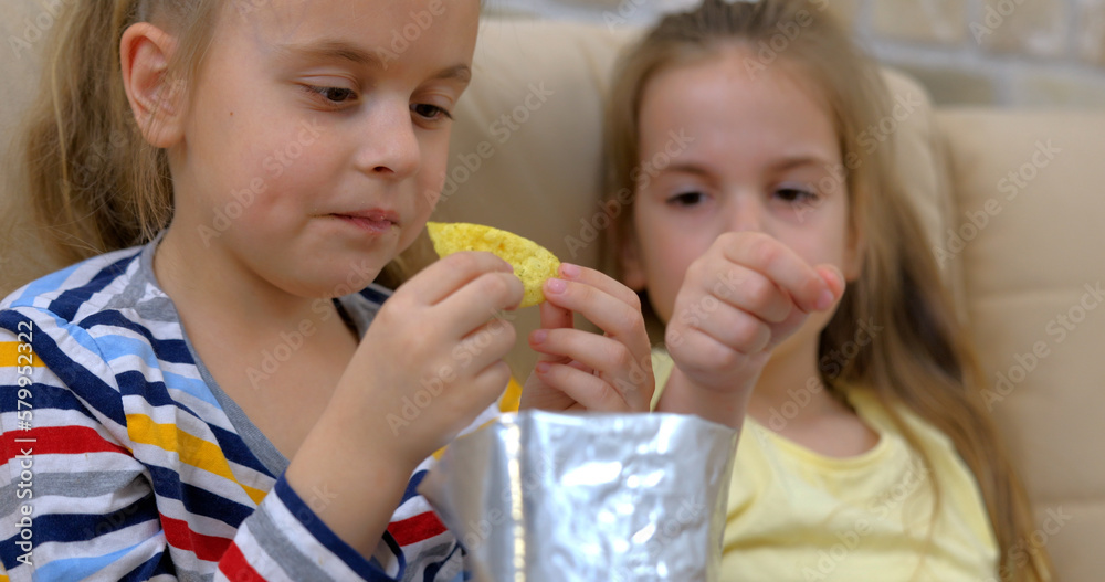 Two cute girls eating chips and watching tv Two cute girls eating chips and watching tv