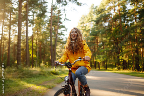 Fototapeta Naklejka Na Ścianę i Meble -  Young woman in yellow coat riding bicycle park. Active day. 