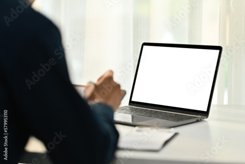 Back view of man worker sitting at office desk with blank screen laptop computer on foreground