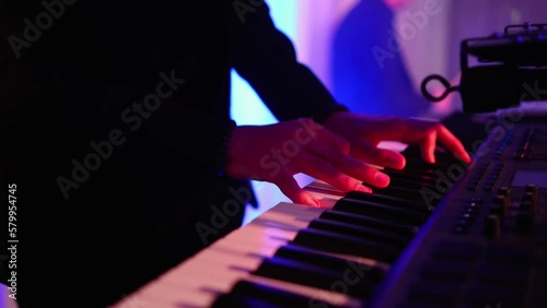 Male hands playing on synthesizer piano. Band at concert stage playing music.