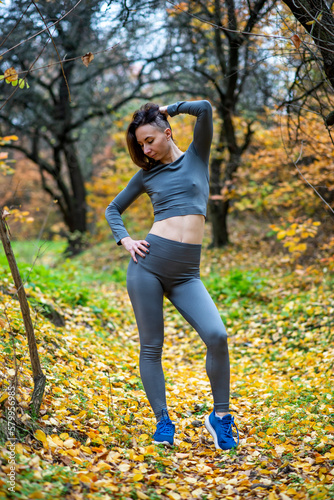 A slender woman in leggings and a crop top poses in the autumn forest.