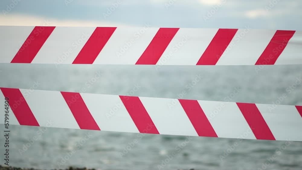 Red white warning tape barrier ribbon swinging in the wind across exotic sea beach background without people. No entry Red White caution tape. No holiday concept, delayed travel, no summer plans Red white warning tape barrier ribbon swinging in the wind across exotic sea beach background without people. No entry Red White caution tape. No holiday concept, delayed travel, no summer plans