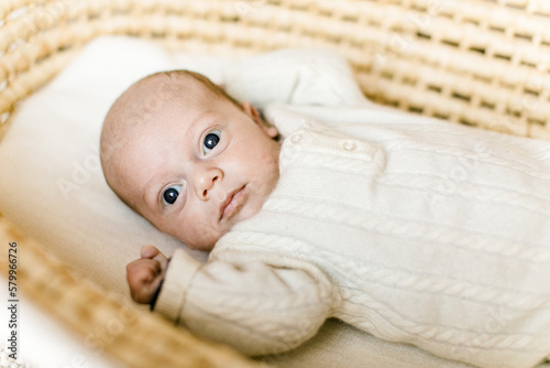 Baby mit großen Augen in weißem Overall in Moseskorb in naturfarben photo
