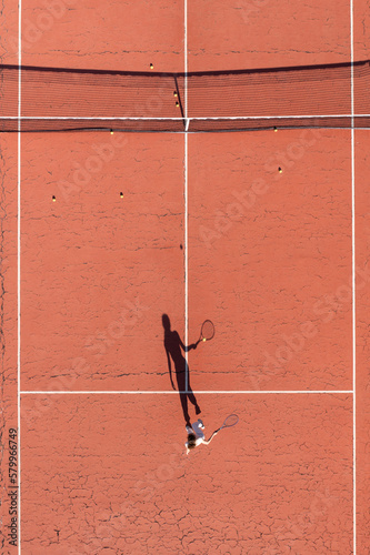 young woman playing tennis on a court with shadow hitting the ball