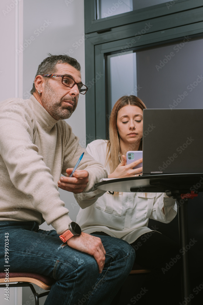 Obraz premium Middle-aged male person thinking about solution for their project problem while his blonde female coworker is chatting on her phone