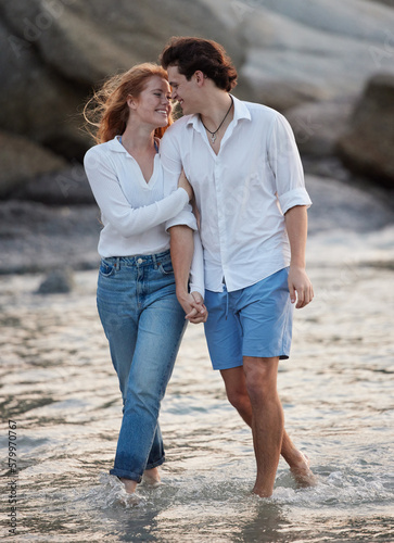 Love, romance and couple in the water at the beach holding hands while on a vacation together. Happy, smile and young man and woman walking in ocean or sea while on romantic weekend trip in Australia