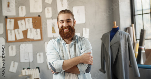 Close-up portrait shot of bearded hipster clothing designer working in his office, looking at camera and positively smiling - small business, fashion concept 