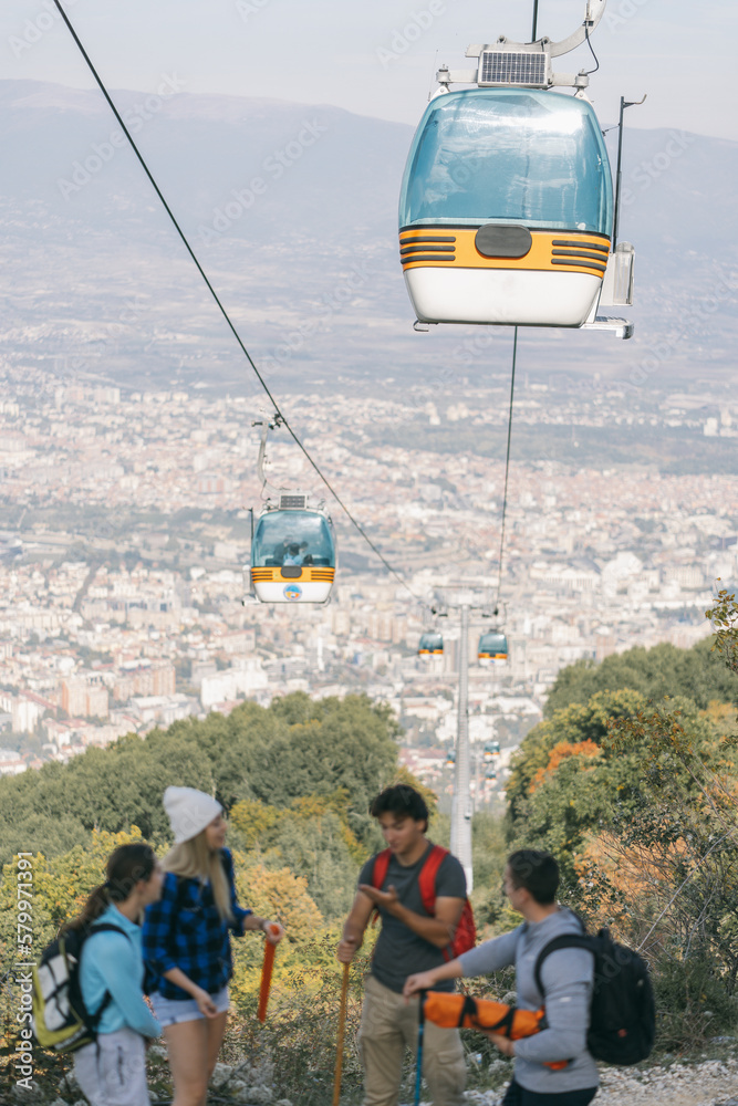 Four hikers standing high in the mountain below the zip line and having a conversation. Panoramic view