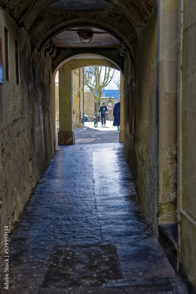 Distant view of senior gray haired woman walking through narrow passage at the old town of Swiss City of Bern on a sunny winter day. Photo taken February 21st, 2023, Bern, Switzerland.