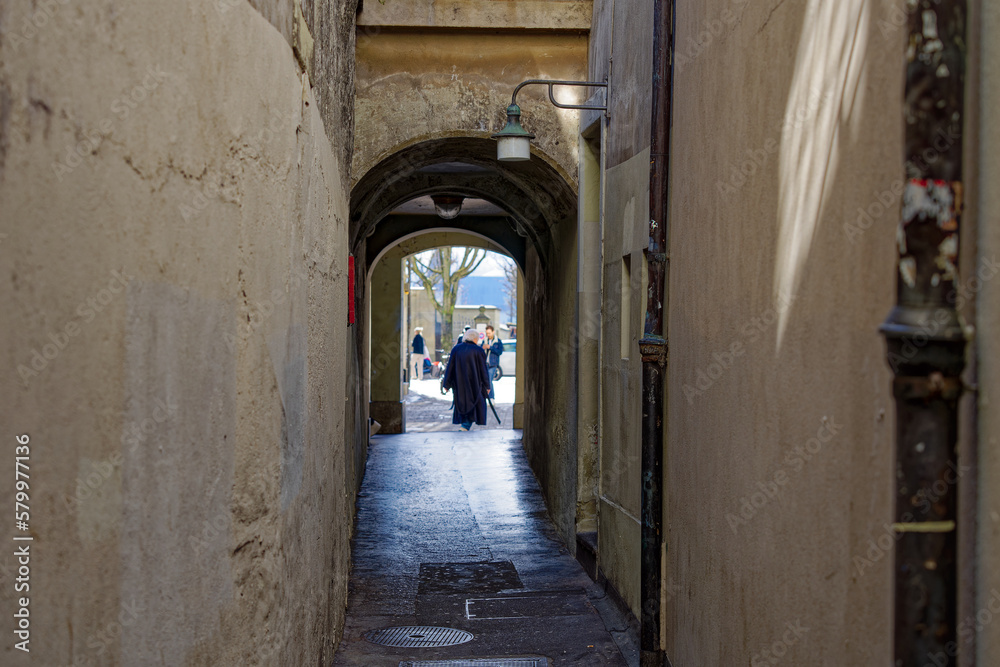 Distant view of senior gray haired woman walking through narrow passage at the old town of Swiss City of Bern on a sunny winter day. Photo taken February 21st, 2023, Bern, Switzerland.