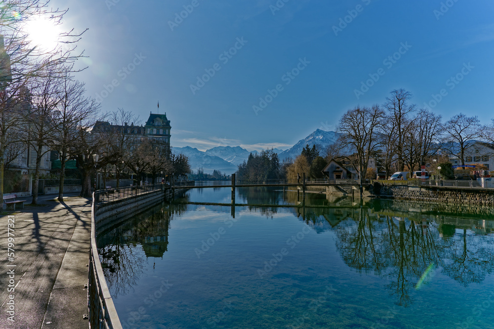 Obraz premium Scenic view of Aare River with lanterns and autumn colored trees and snow capped mountains of Swiss Alps in the background at Swiss City of Thun. Photo taken February 21st, 2023, Thun, Switzerland.