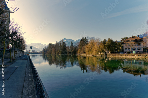 Scenic view of Aare River with lanterns and autumn colored trees and snow capped mountains of Swiss Alps in the background at Swiss City of Thun. Photo taken February 21st, 2023, Thun, Switzerland. © Michael Derrer Fuchs