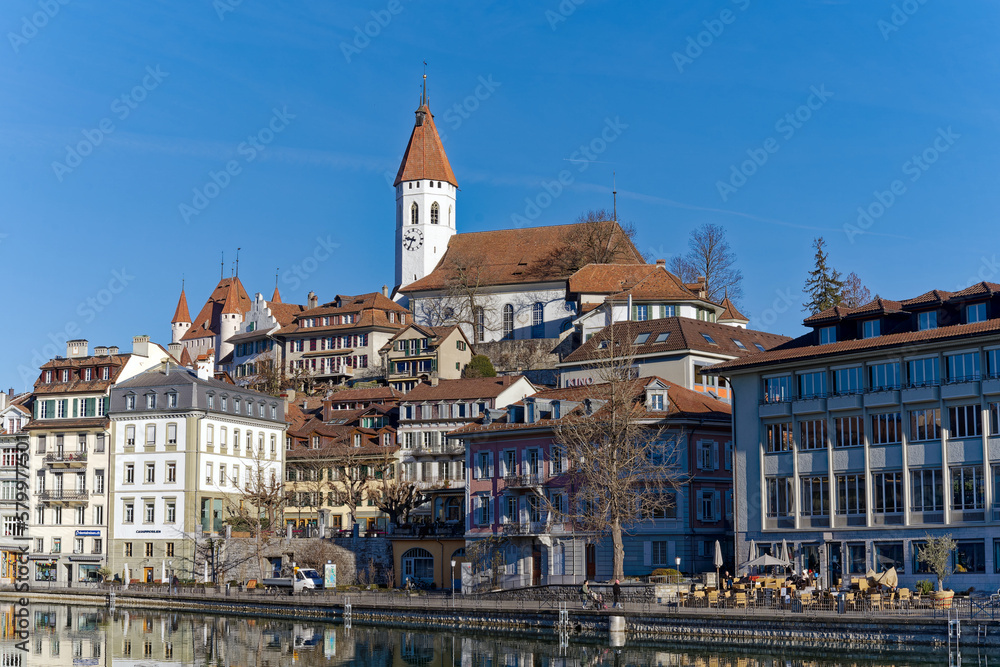 Naklejka premium Old town of City of Thun with church and castle on a hill in the background on a sunny winter day. Photo taken February 21st, 2023, Thun, Switzerland.