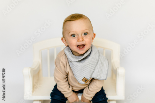 Lachender kleiner Junge in neutralen Farben sitzt auf weißer Holzbank